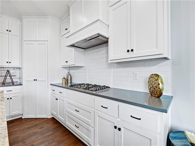 Kitchen with white cabinets, stainless steel gas stovetop, dark hardwood / wood-style flooring, and decorative backsplash
