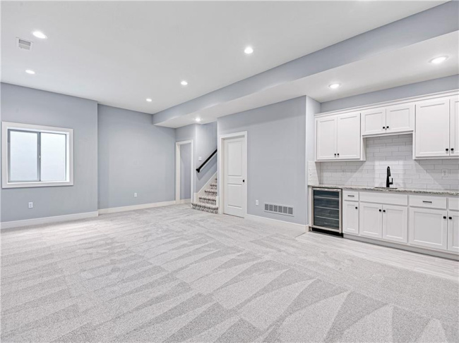 Unfurnished living room featuring light carpet, wine cooler, and sink